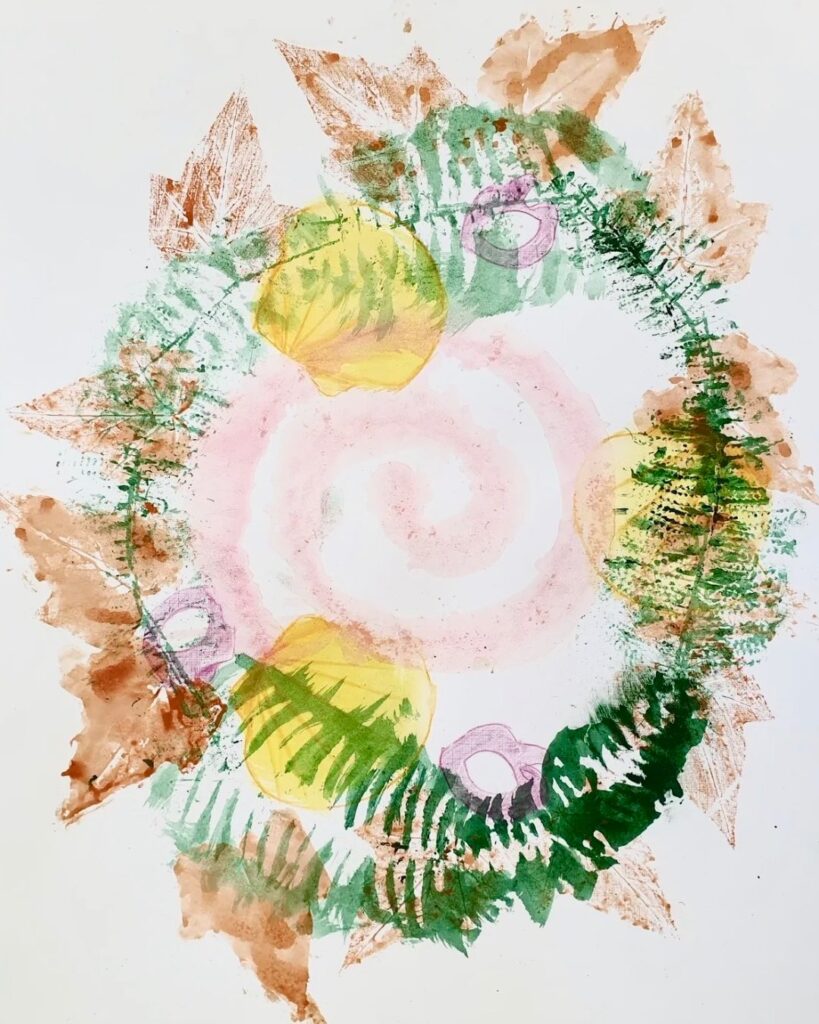 Circular mixed-media artwork: spiral centre surrounded by leaf and fern prints in green, yellow and brown.