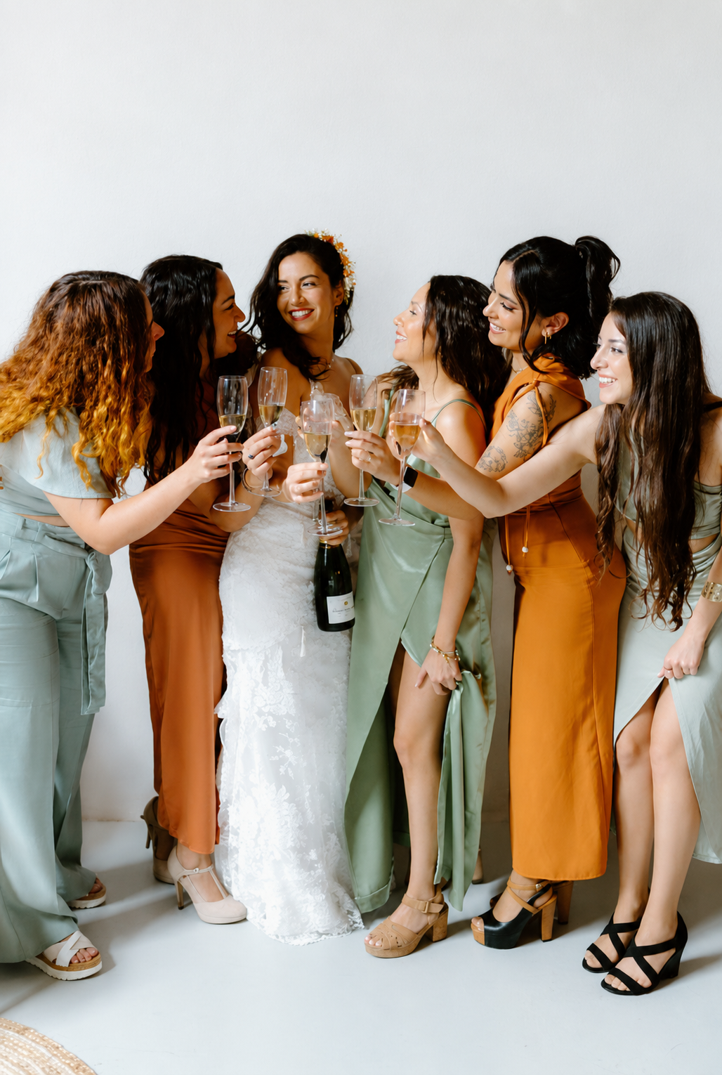 A bride and friends raising champagne glasses against a plain white wall