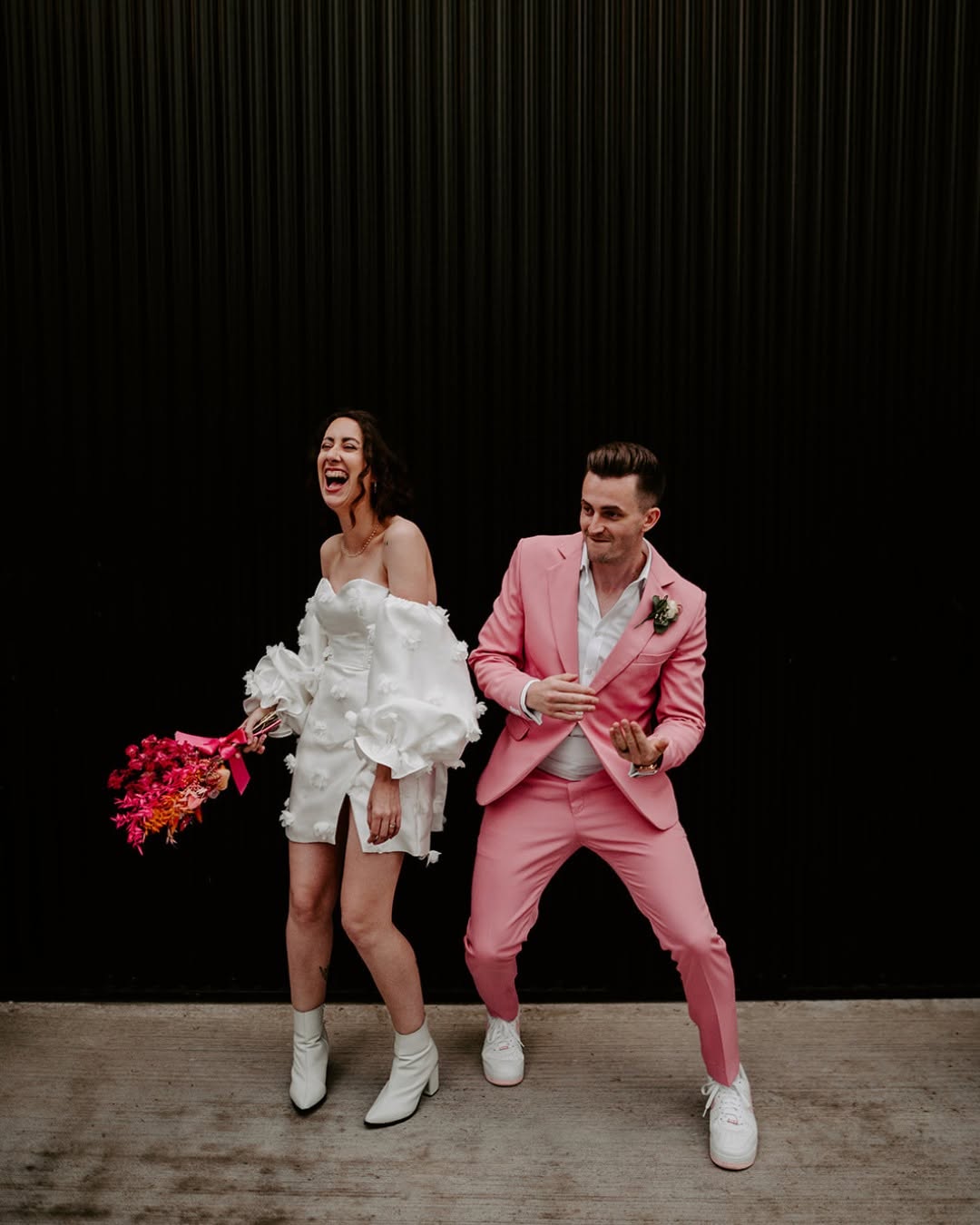A couple laughing together in a white dress and pink suit
