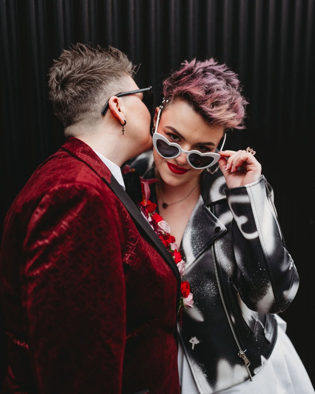 A couple sharing a kiss, wearing red velvet, silver and heart-shaped sunglasses
